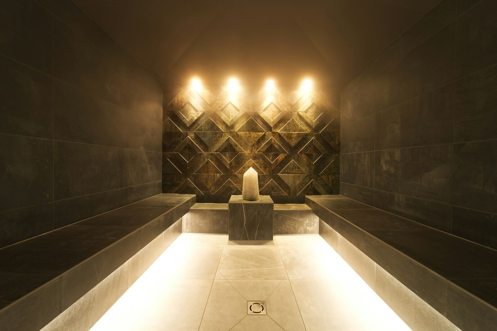 A candle-lit niche glowing warmly between dark stone benches