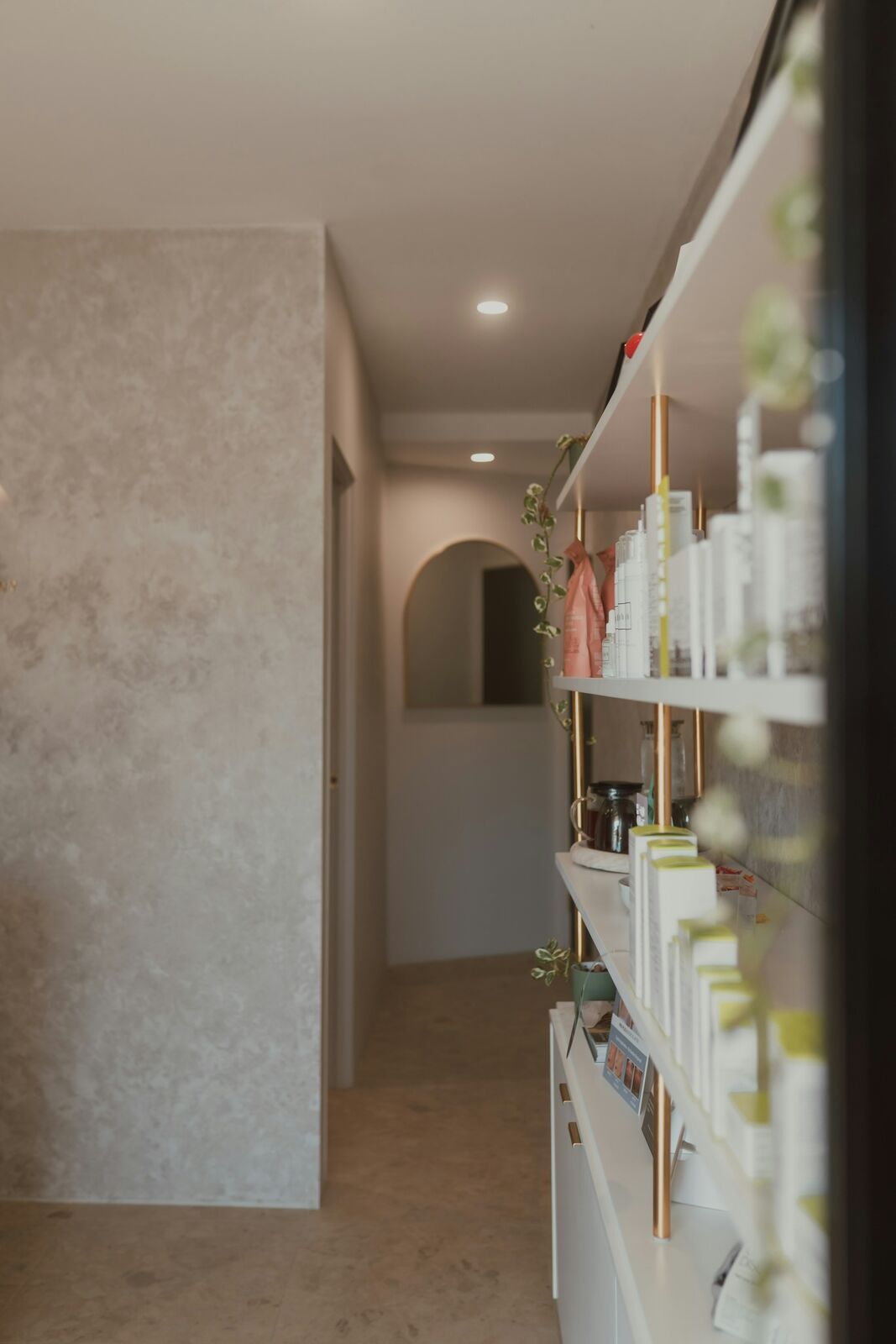 Softly lit shelves of skincare along a plaster hallway ending in an arch