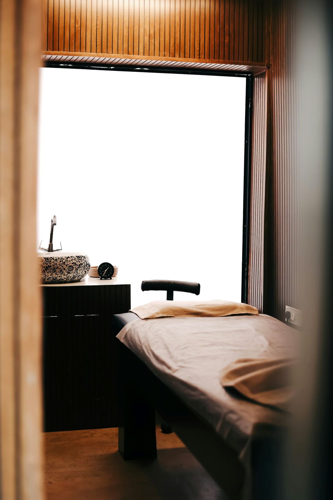 A quiet treatment room with a beige-draped bed beside a bright window