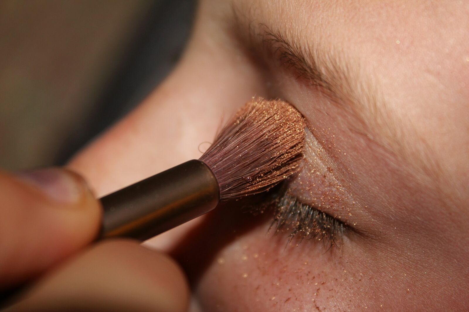 A soft brush blending warm eyeshadow onto a closed eye